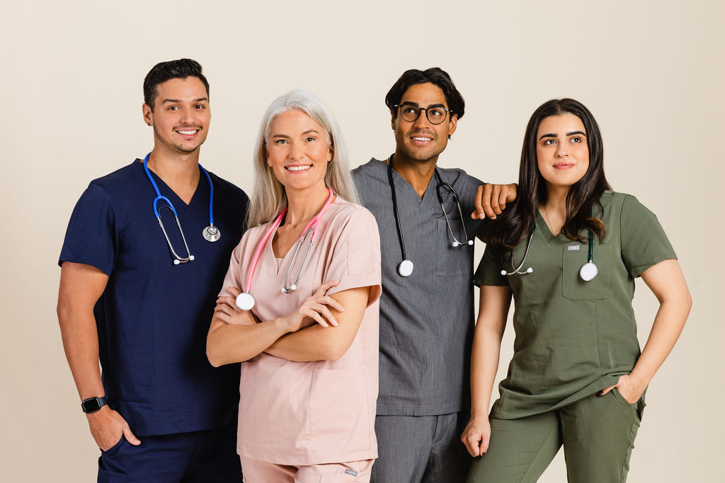A group of 4 nurses in colorful scrubs standing together smiling at the camera and away from the camera. 