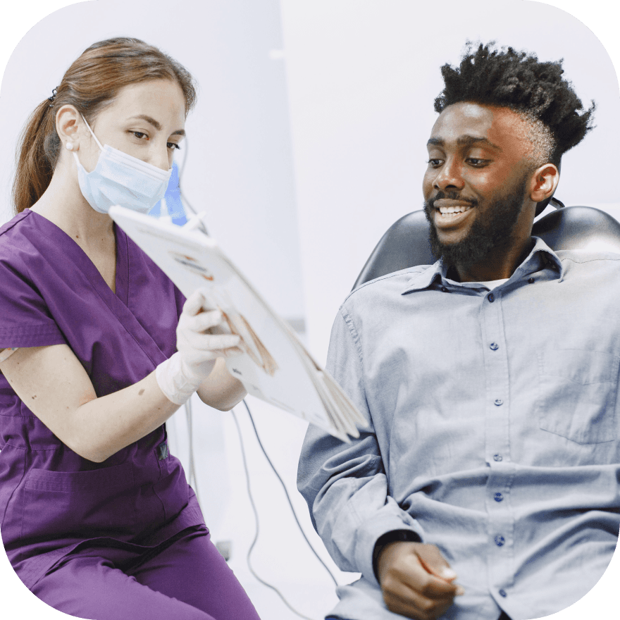 A dentist in purple scrubs showing a dental X-ray to a patient, both engaged in the consultation.