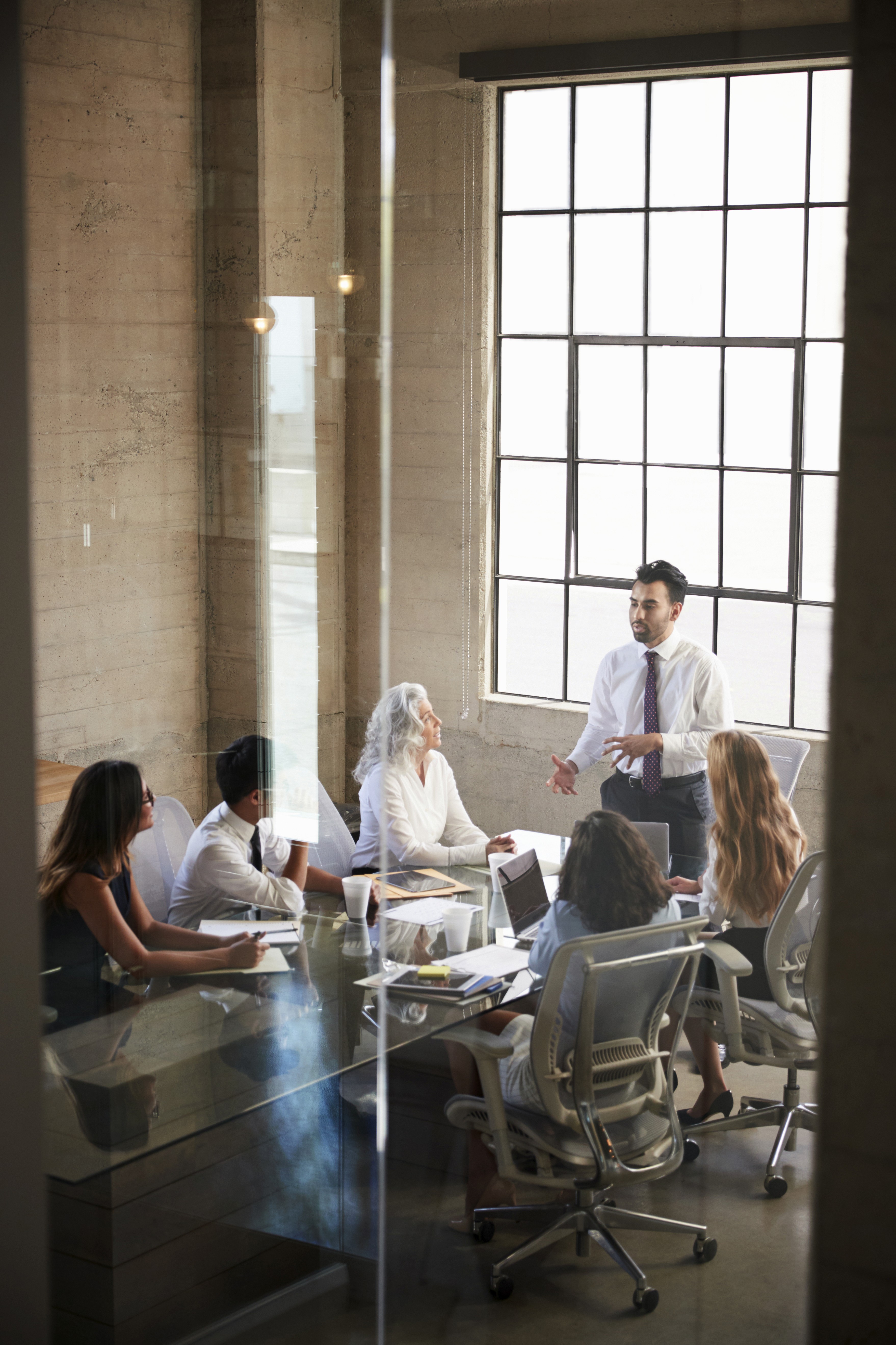 Businessman addressing colleagues in meeting seen through window