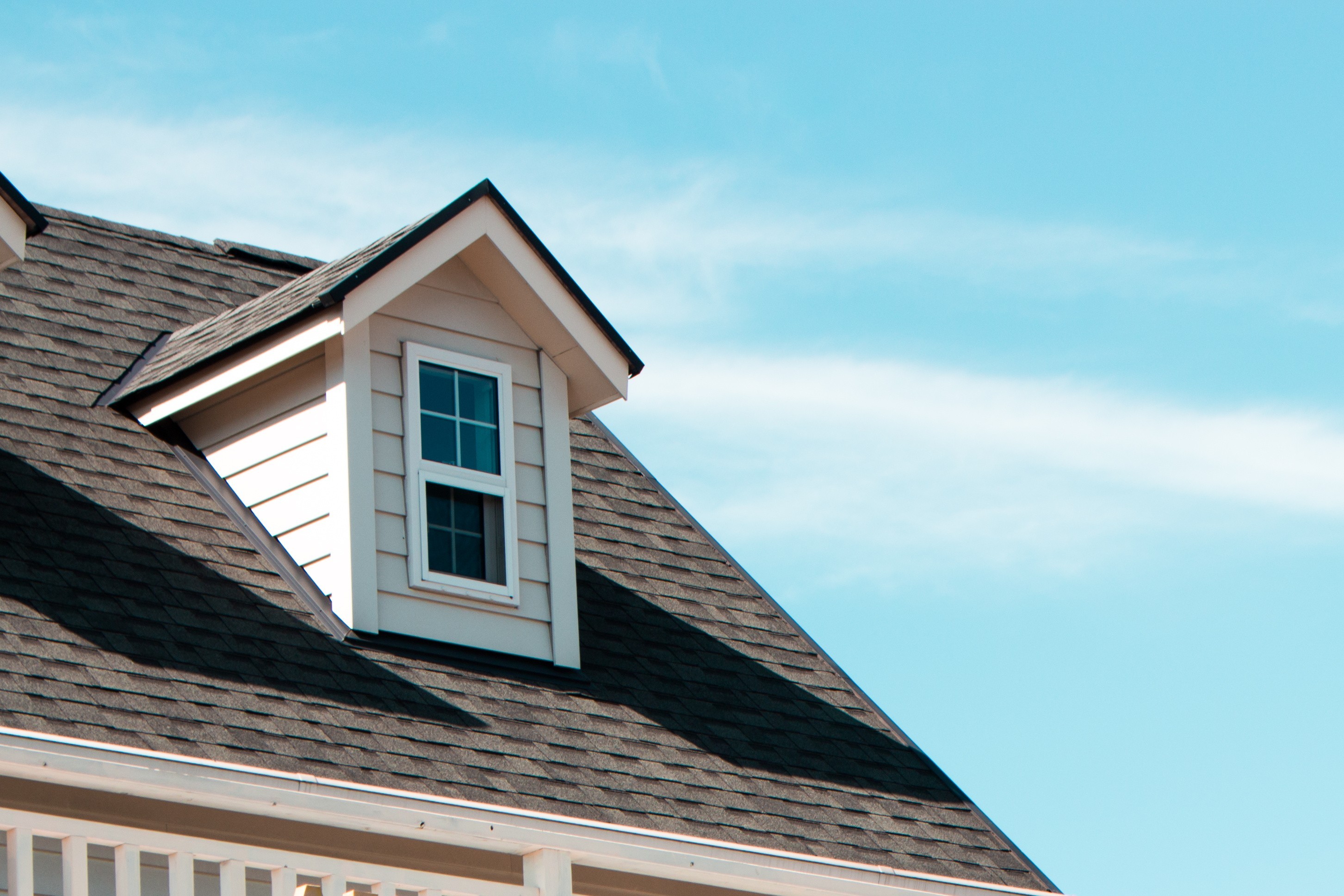 Residential asphalt shingle roof with dormer window on a home in St. Louis, Missouri, under clear blue skies — ideal for roofing inspection and repair services.
