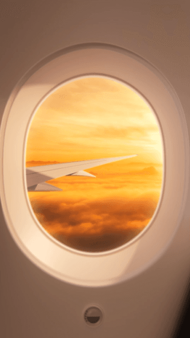 A view of an airplane wing over golden clouds through a circular Turkish Airlines cabin window