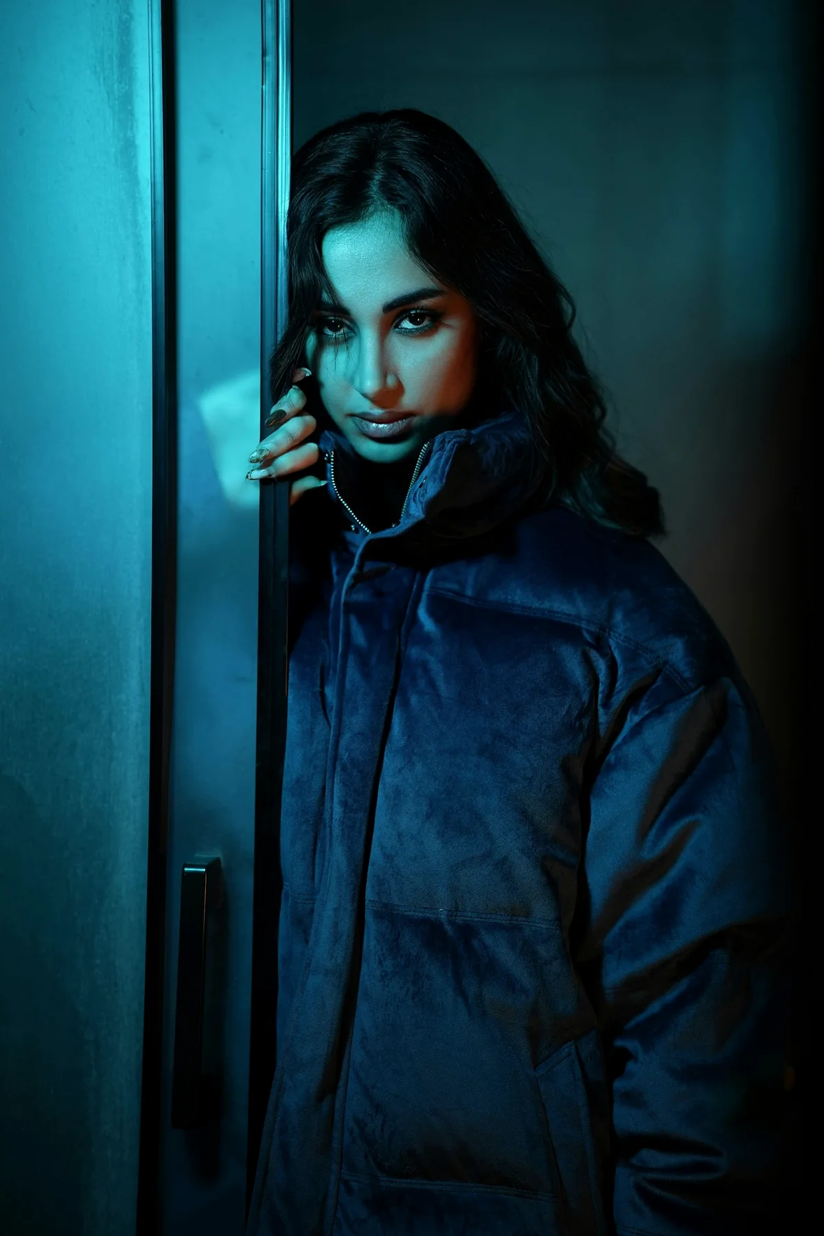 Model in a blue puffer jacket lit by cyan light