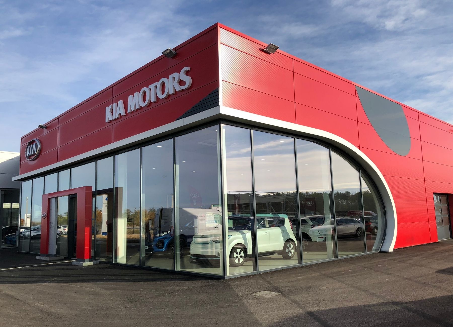 Façade arrondie d’un bâtiment commercial rouge avec bardage métallique et enseigne.