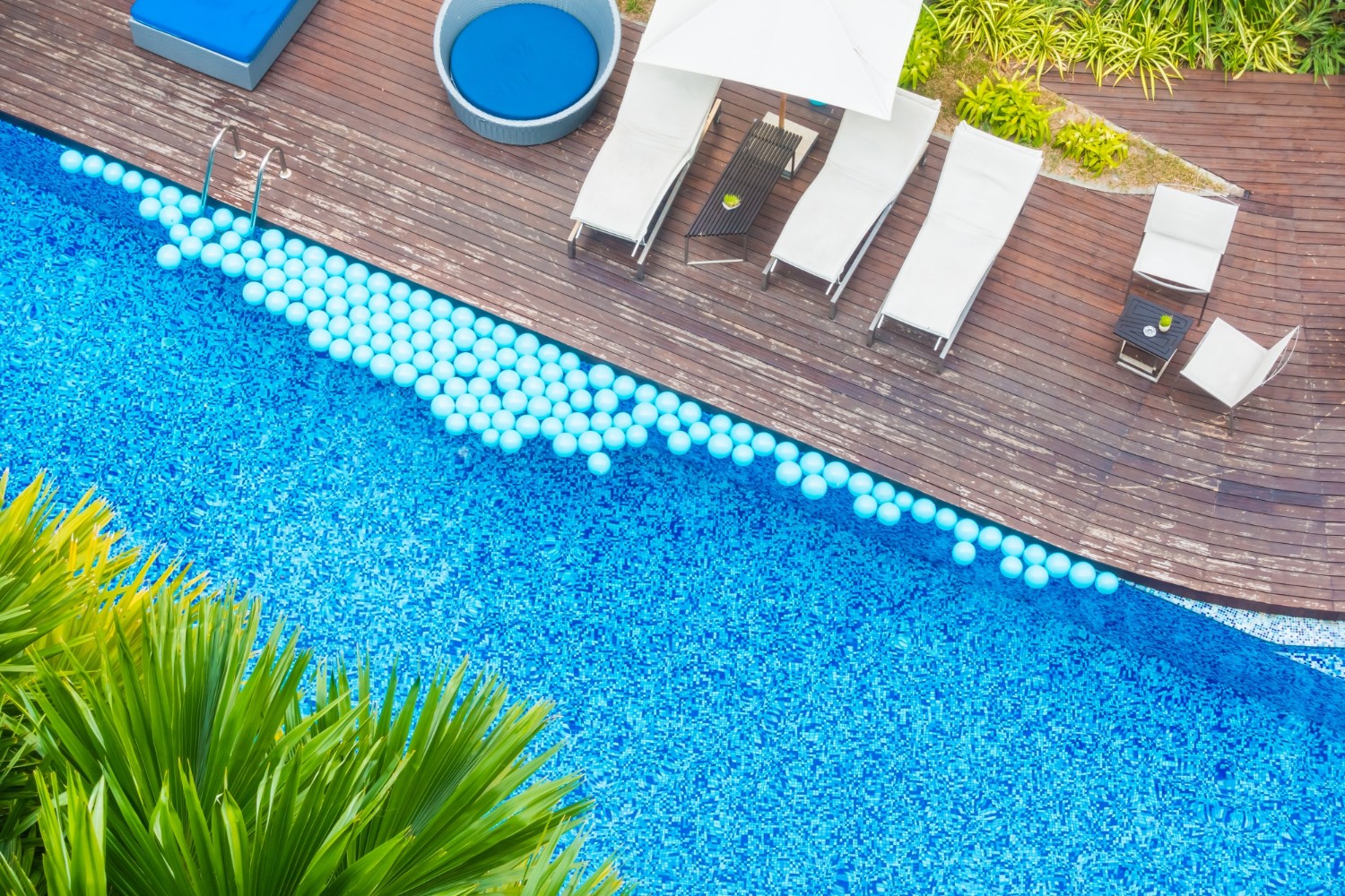 Aerial view of a commercial pool with white sun loungers and umbrellas arranged on a timber deck.