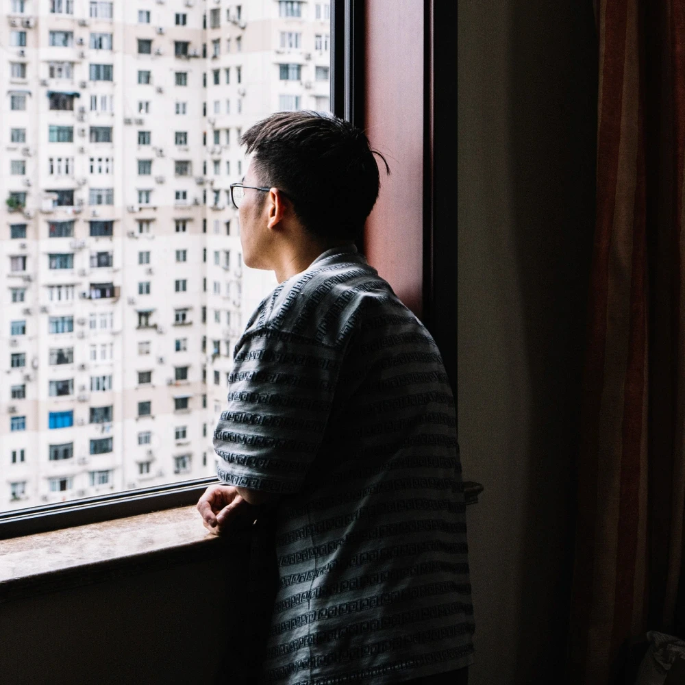 Asian man staring out of window, apartment blocks in background