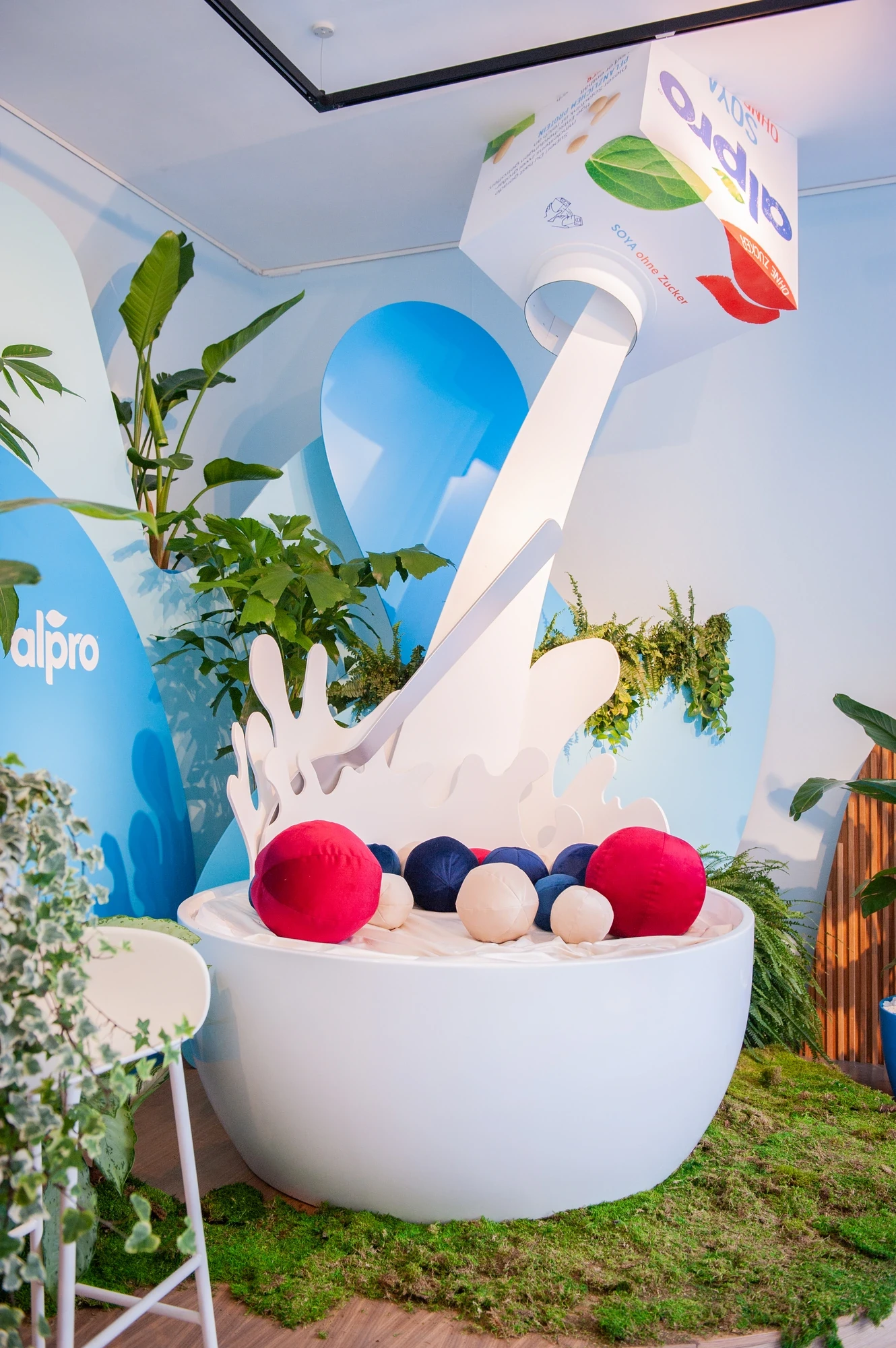 Oversized Alpro installation showing a giant bowl with red and blue plush berries and a tilted Alpro carton pouring milk, surrounded by greenery.