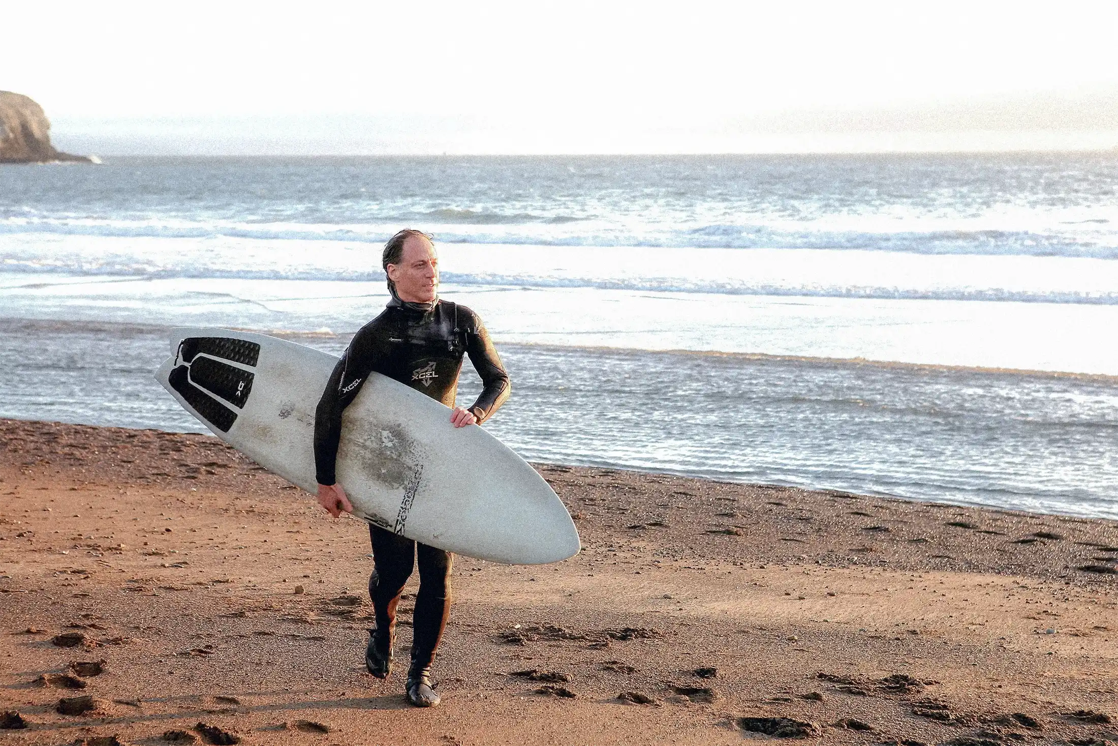 Dr. Brad Jacobs carries a surfboard along the beach after a surf session.
