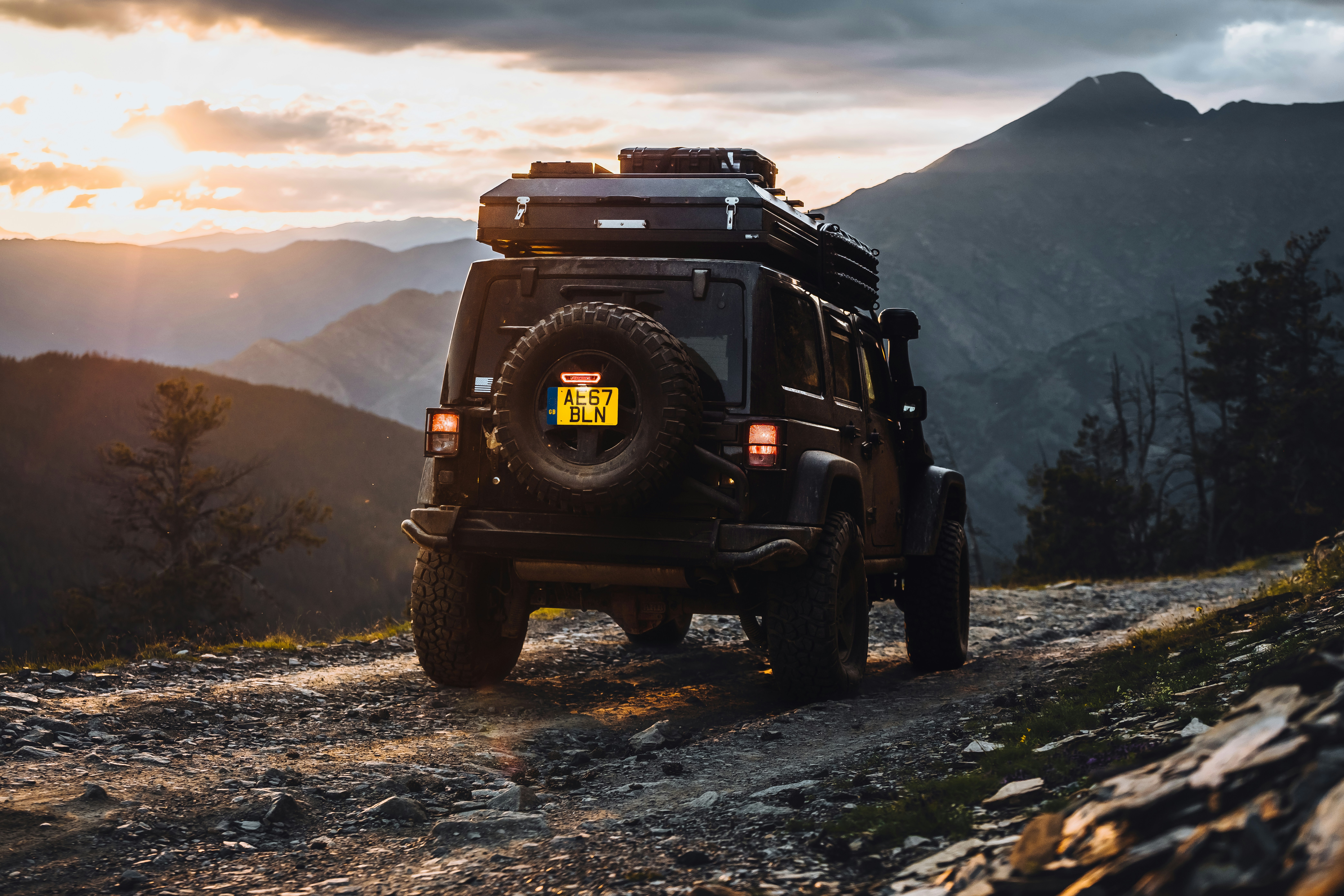 Off-road jeep on a mountain path at sunset.