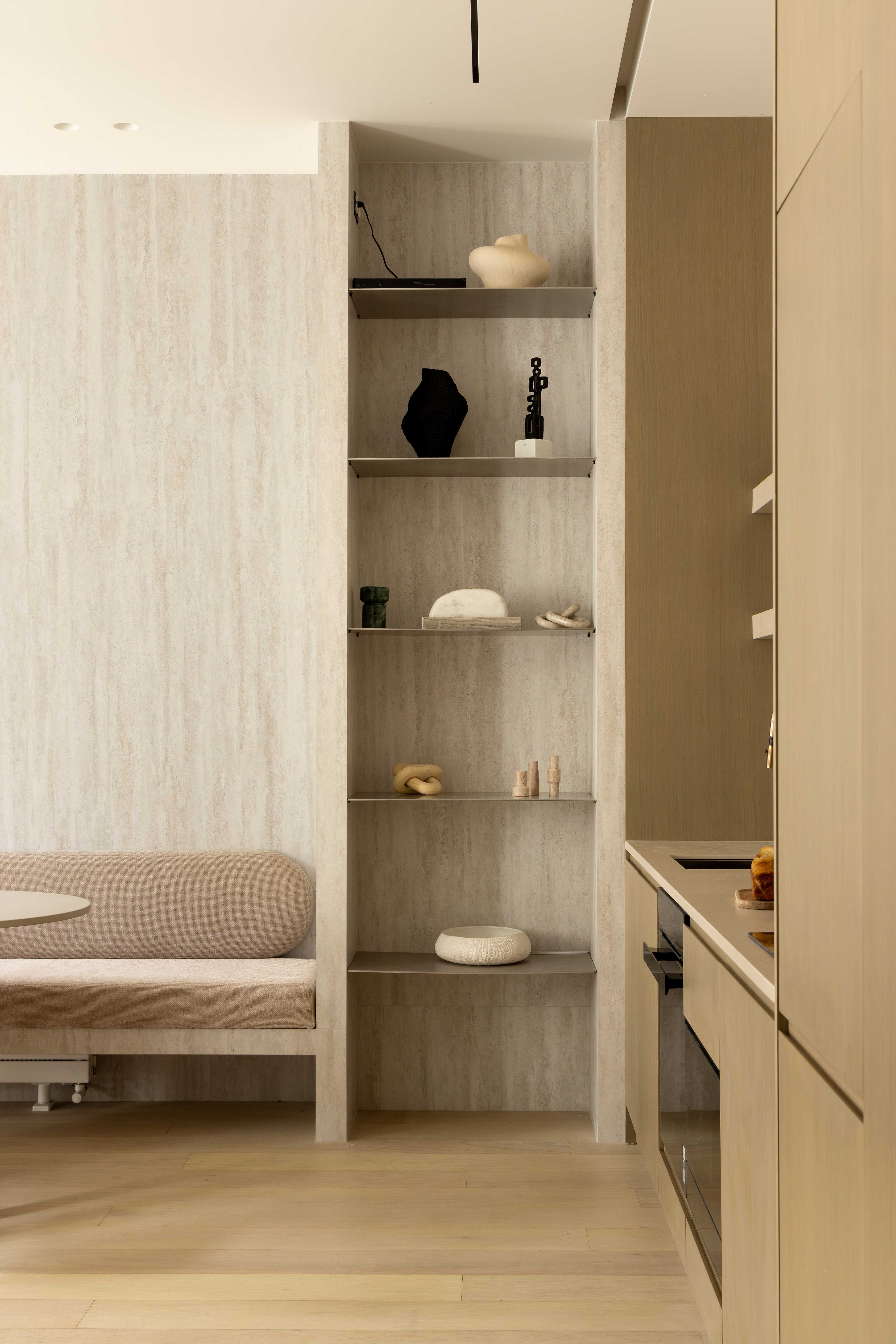 Etageres en travertin avec objets decoratifs noirs et beiges, banquette arrondie et cuisine en bois clair