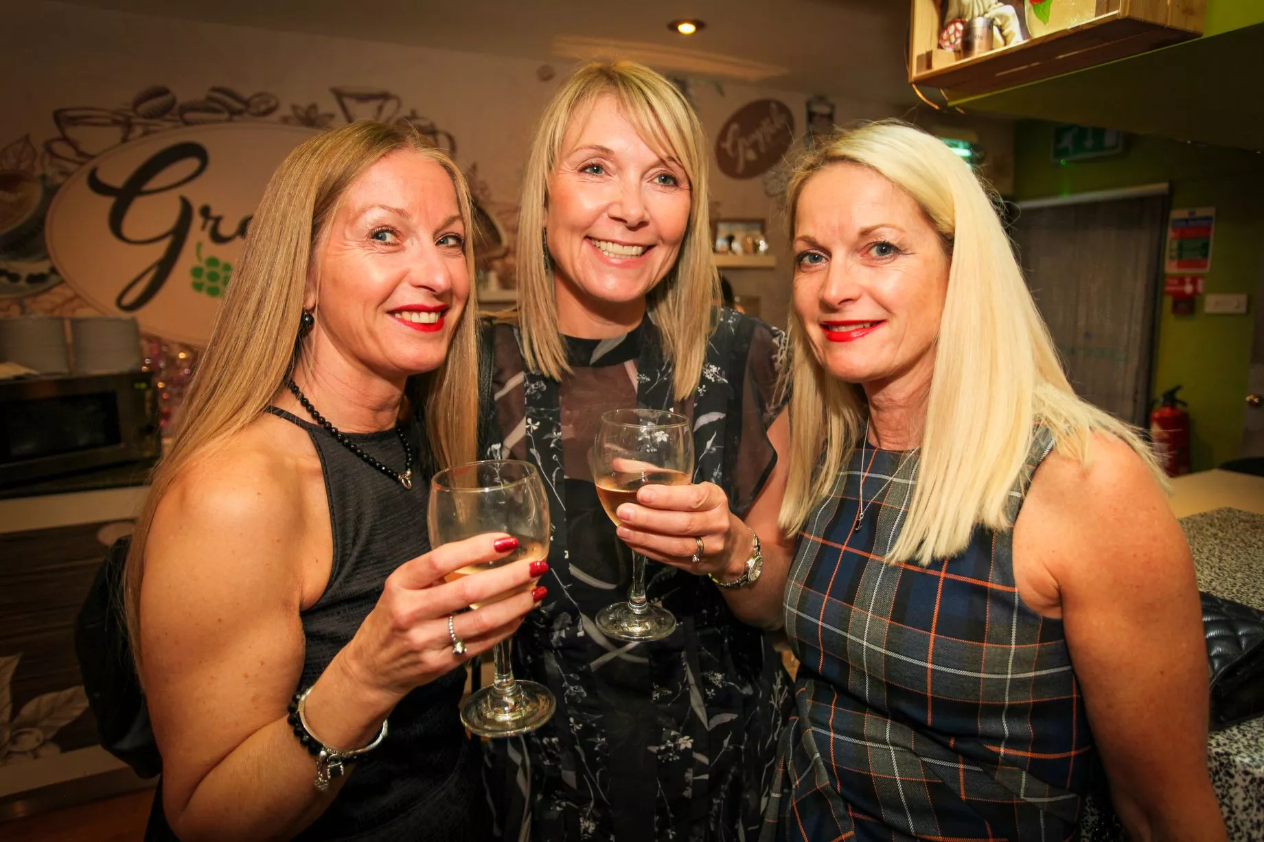 Three women enjoying a drink in a bar smiling at camera