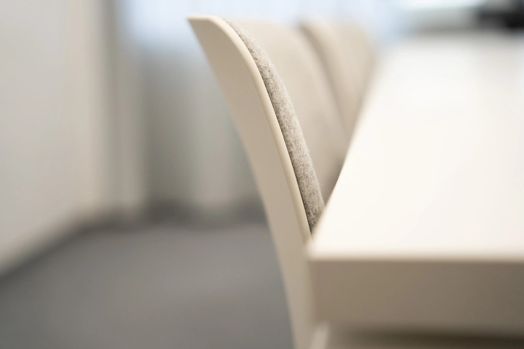 Close-up of a row of cream chairs with grey felt seat pads along a white high table at NFON, photographed with shallow depth of field.