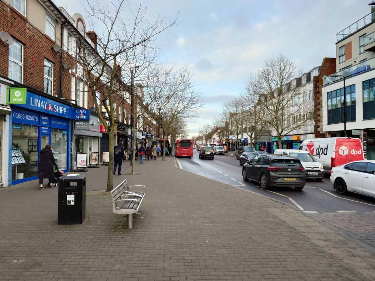 A smiling man with curly hair is sitting at a desk, looking at the camera, with a laptop and a lamp in the background.