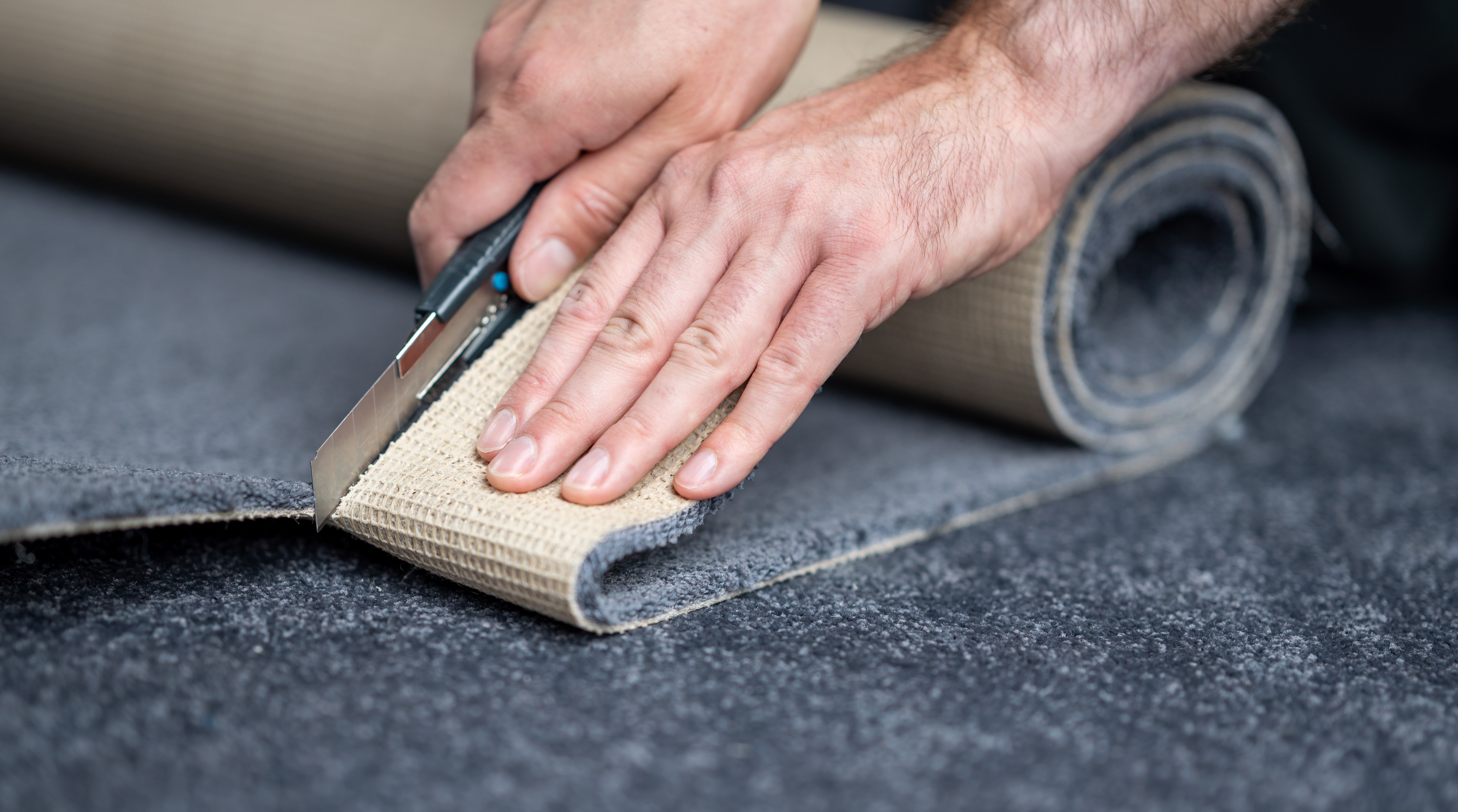 Installer trimming broadloom carpet from the roll with a carpet knife