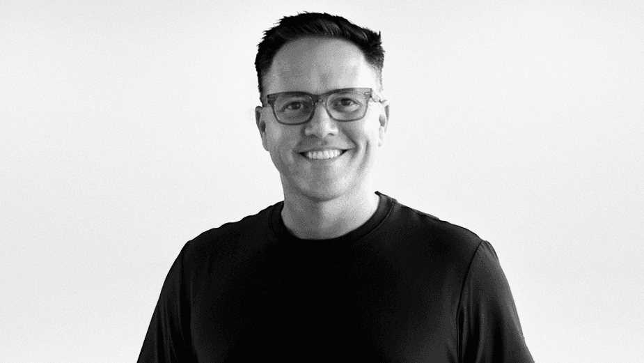 Smiling person with curly hair, wearing a black shirt, against a warm, dark background.