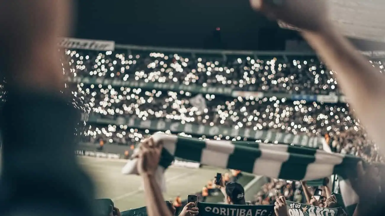 Football fans raising a scarf in solidarity, with a backdrop of twinkling lights from mobile phones in a packed stadium, capturing the vibrant energy and community spirit that characterises the unforgettable experience of live football matches, reflecting the essence of grassroots sports as discussed in an article about amateur football tournaments.