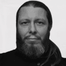 Portrait of a woman with long, smooth hair swept to the side, in a dark t-shirt, on a plain background.