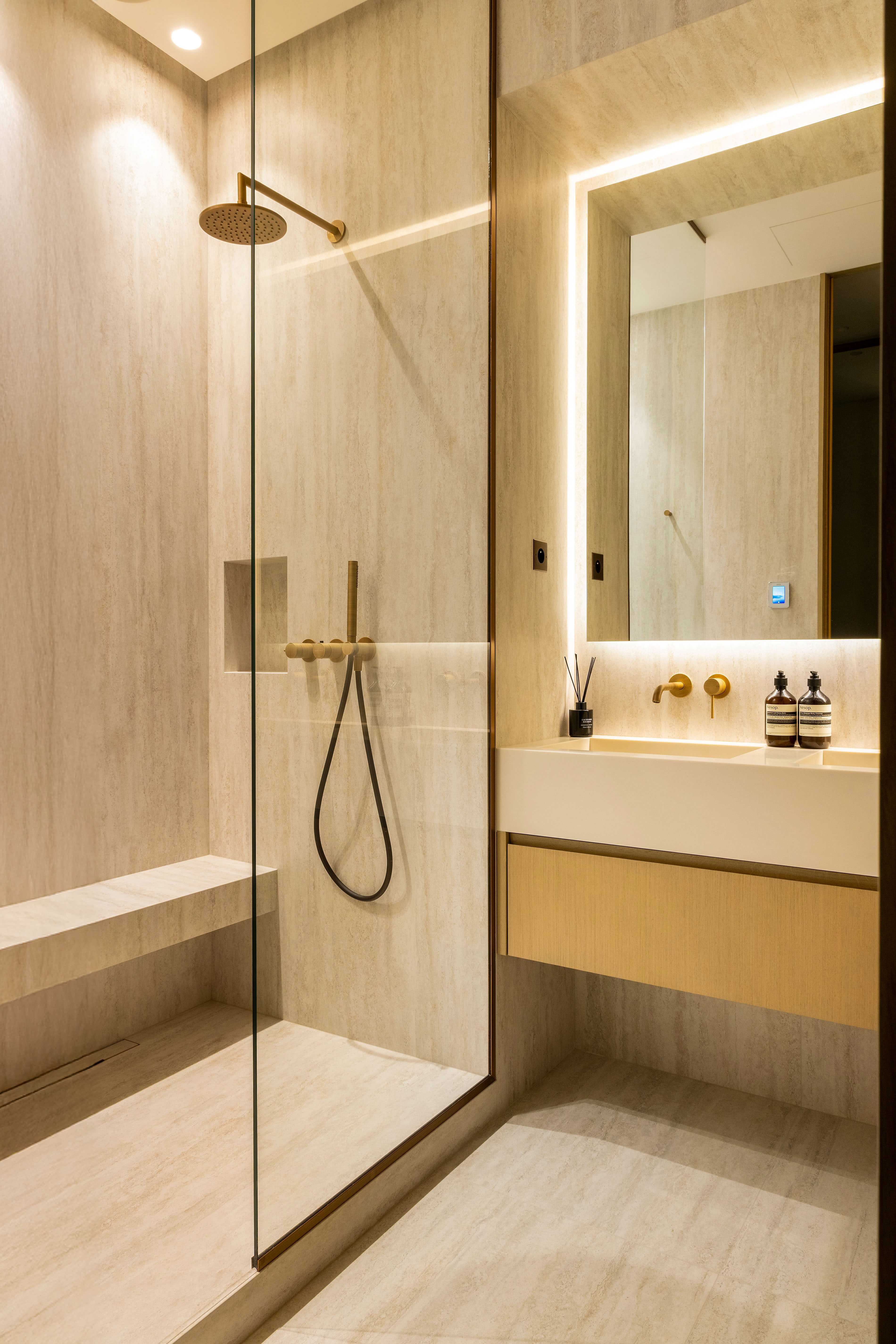 Salle de bain avec douche italienne en pierre, robinetterie dorée, miroir rétroéclairé et vasque