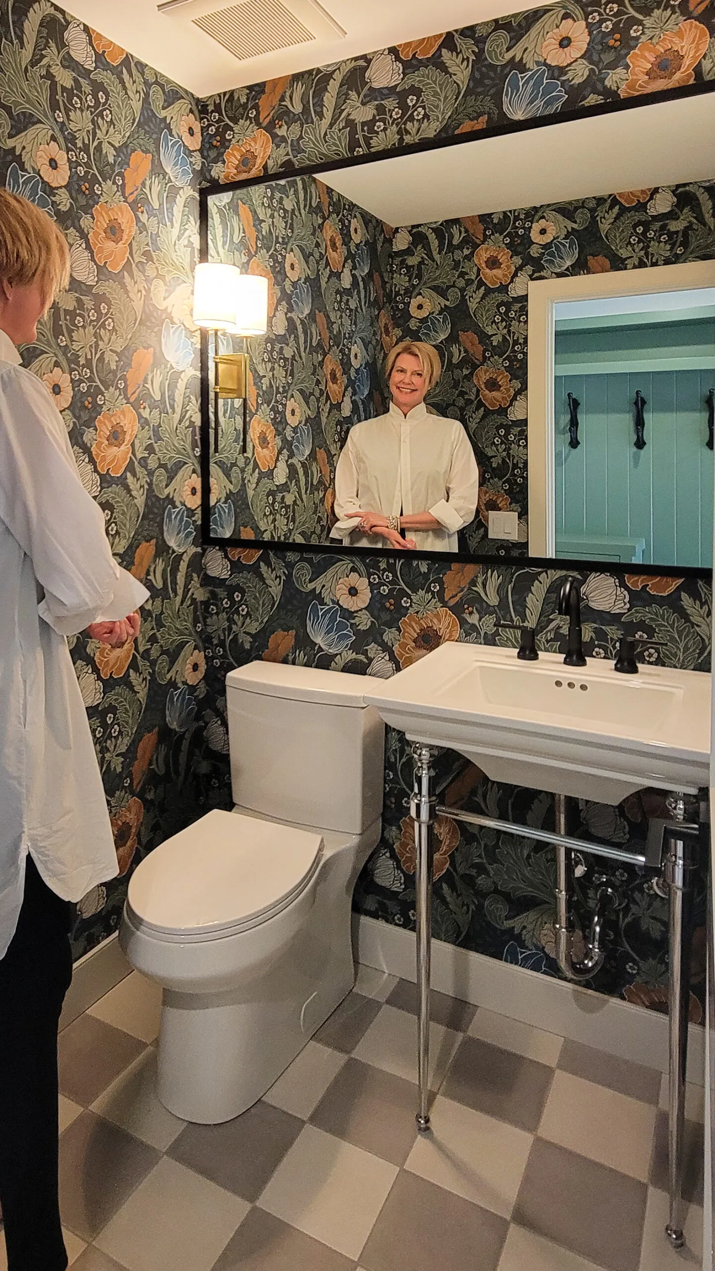 Image of blond woman in powder room with floral wallpaper.