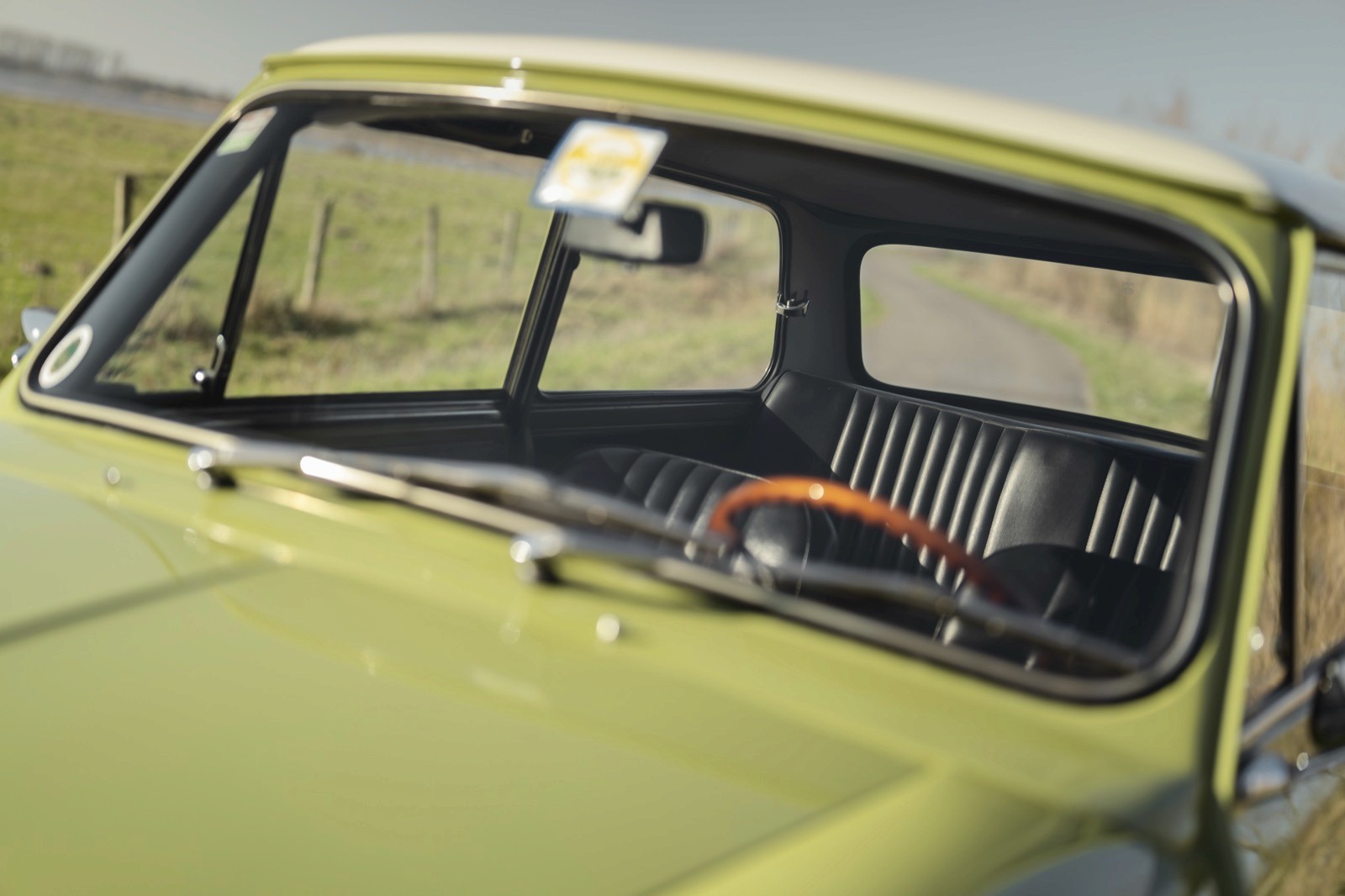 Close-up view of a vintage car's dashboard and windshield with a sunny landscape outside.