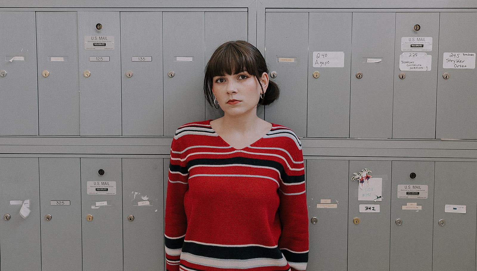 Model in striped red sweater stands in front of grey mailboxes at Revelator Studio in Shreveport for a 90s-inspired photoshoot.