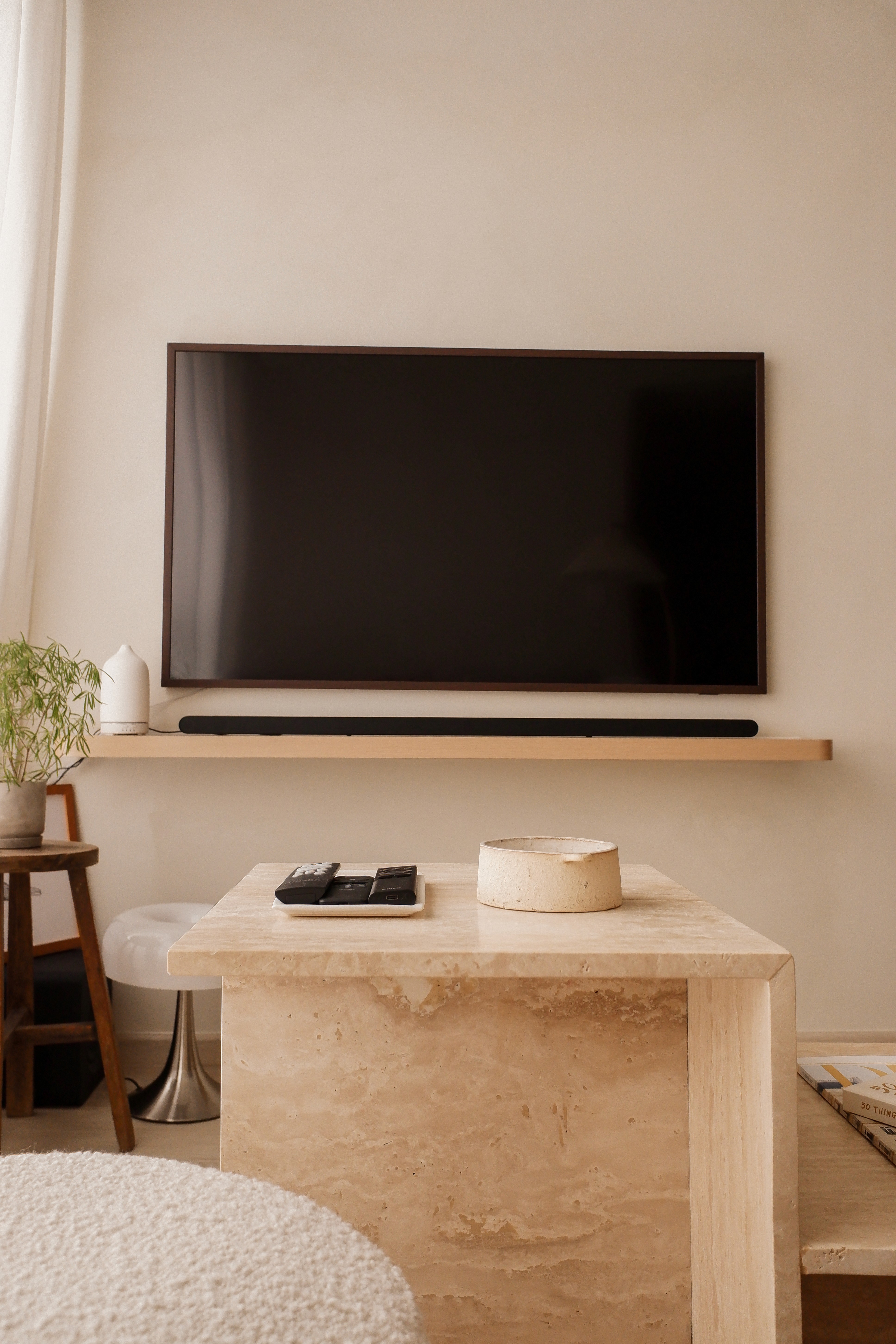 Modern minimalist living room with wall-mounted TV, travertine coffee table, and floating shelf, home renovation by Persqft Singapore