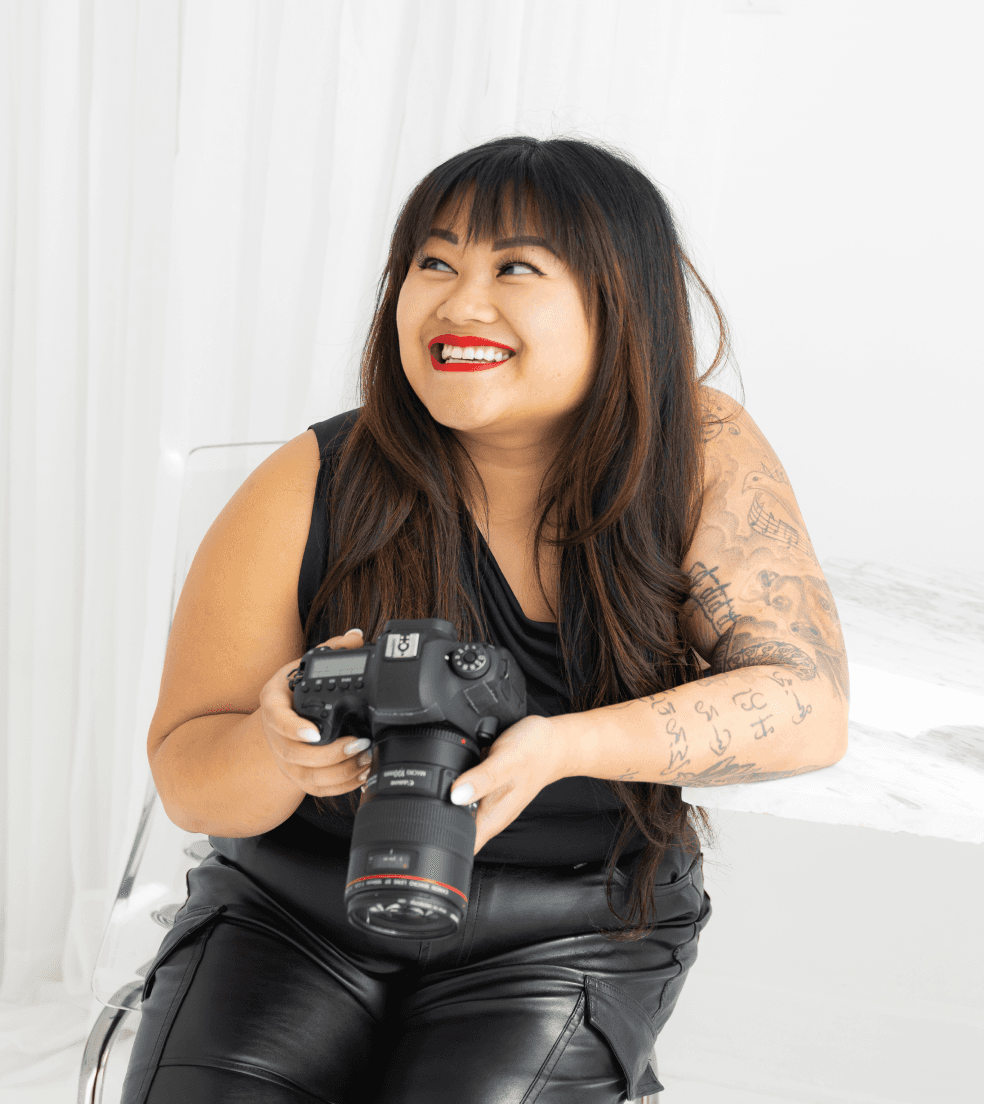 Filipino photographer smiling & holding her camera during a branding photoshoot in a Winnipeg studio