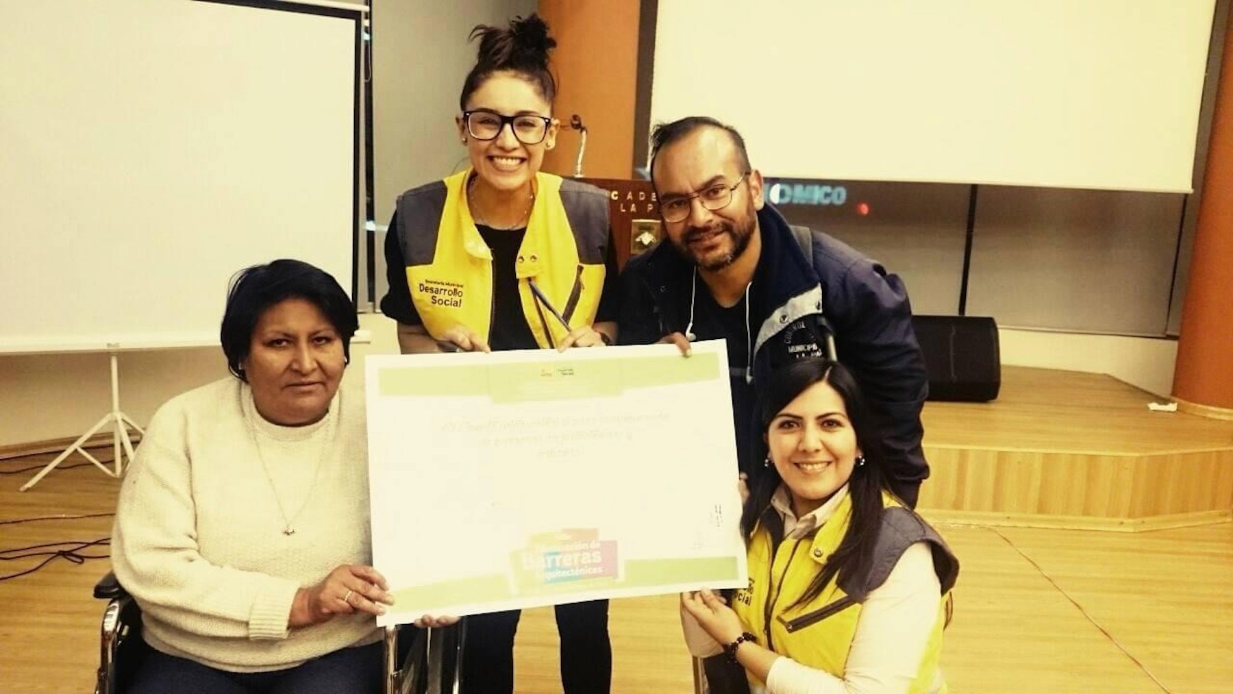 Daniela Jines and colleagues present a recognition certificate to a seated participant during a community development program.