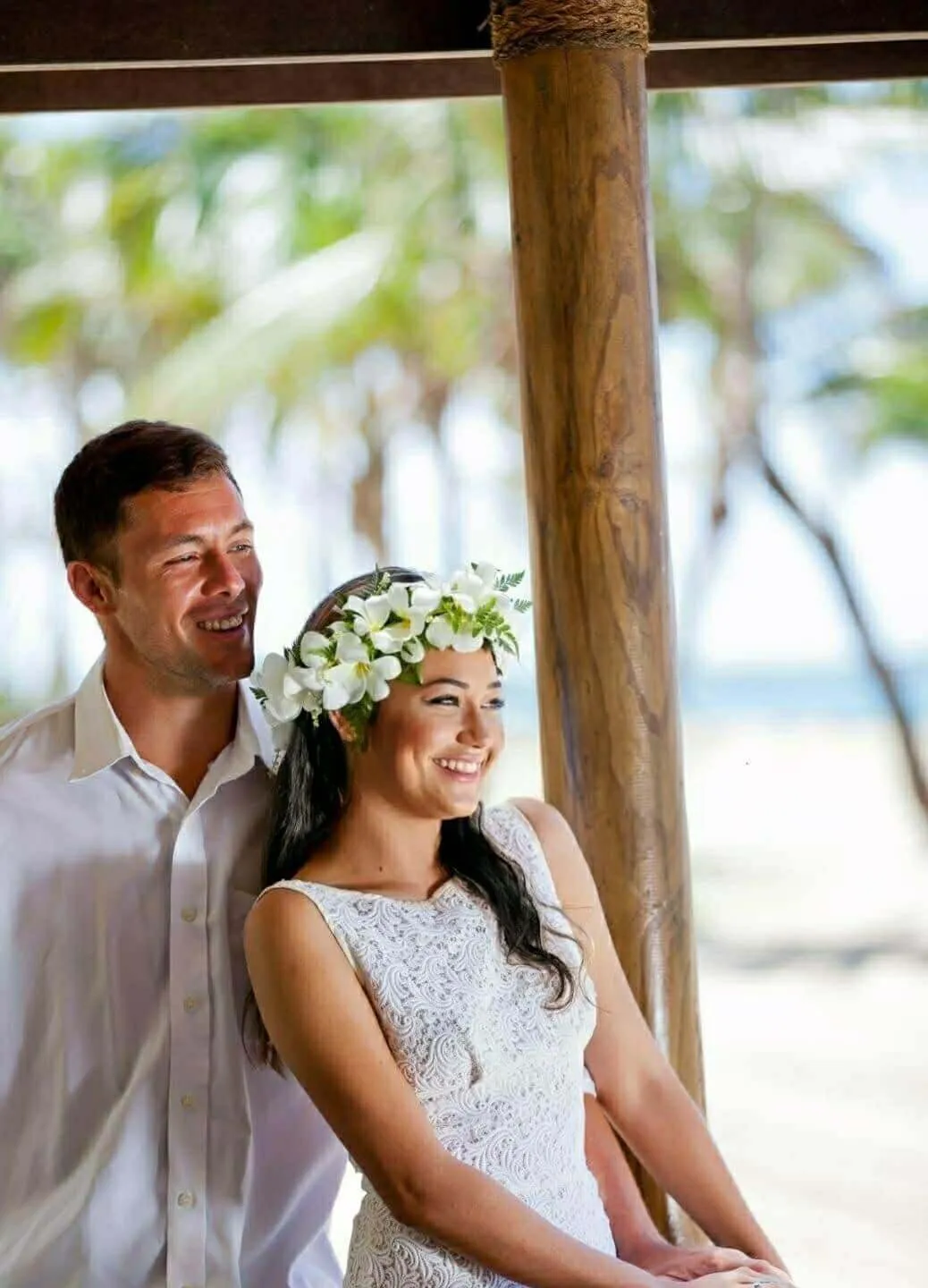 Smiling couple, the woman in a white dress and floral crown, in a tropical wedding setting at Uprising Resort in Fiji.