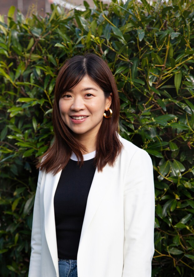Smiling blonde woman with freckles in a white shirt, arms crossed, minimalist studio portrait.