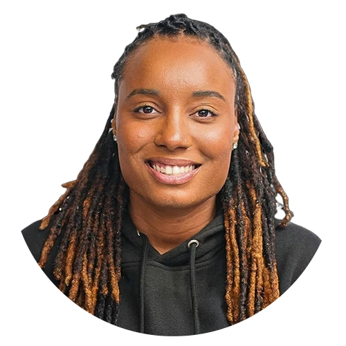 A smiling man with short hair stands with arms crossed, wearing a dark shirt against a neutral background.