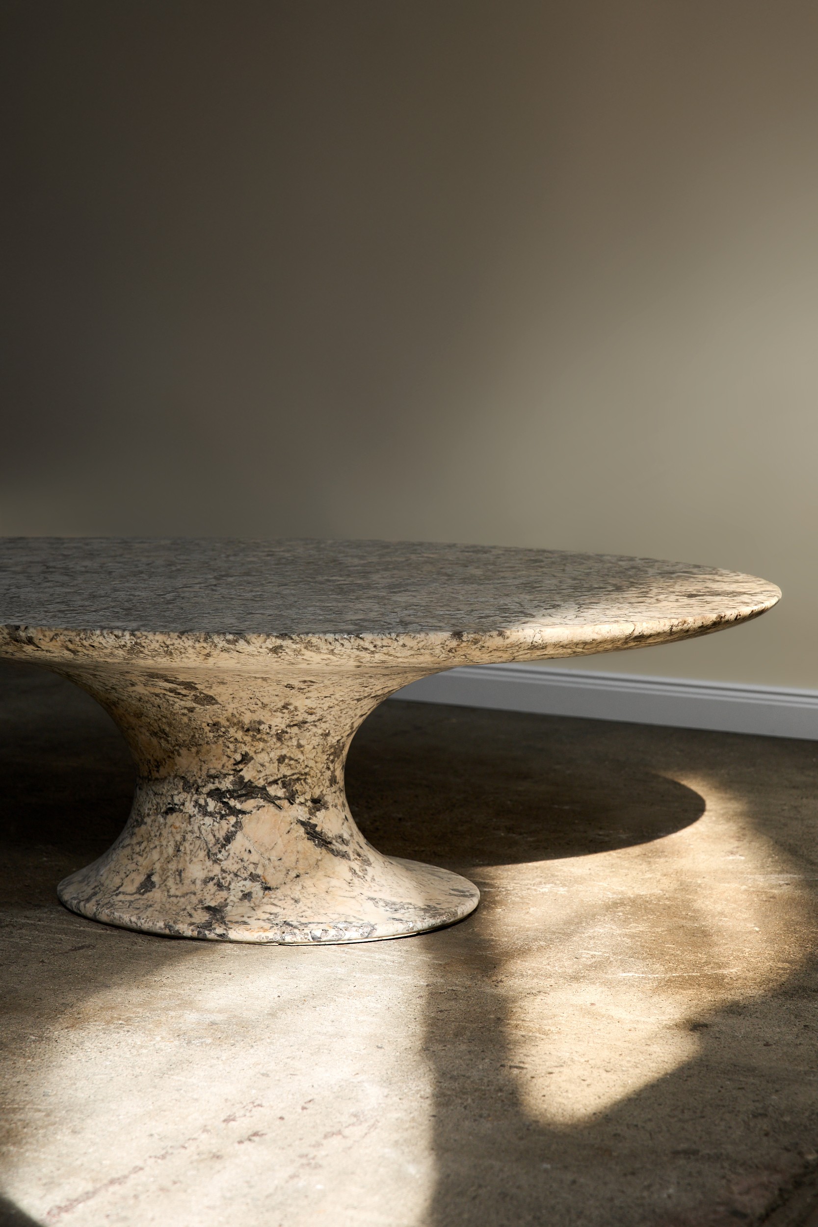 Runder Tisch aus hellem Stein mit dunkler Maserung und massivem Sockel.