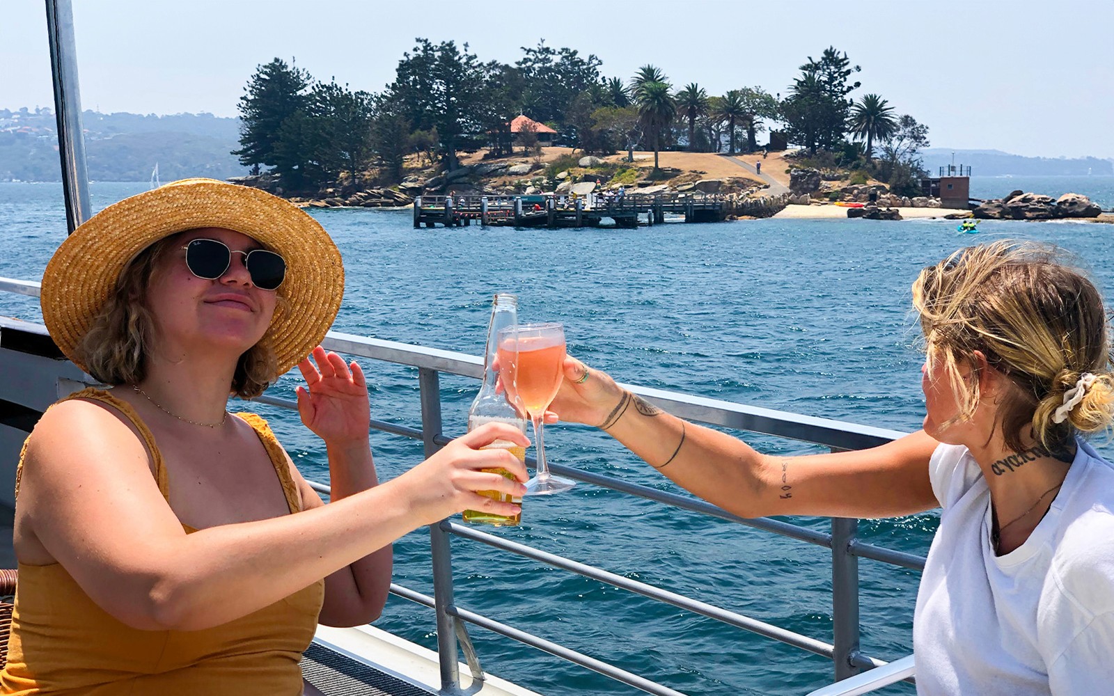 Personas brindando con bebidas en un crucero turístico por el Puerto de Sídney con vista a la isla.