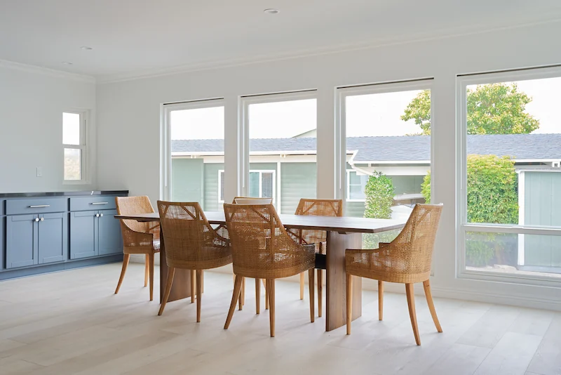 Dining space with a wooden table and chairs, blue cabinets, and open wall shelves in Costa Mesa Exterior Remodel. Photo by Todd Huge.