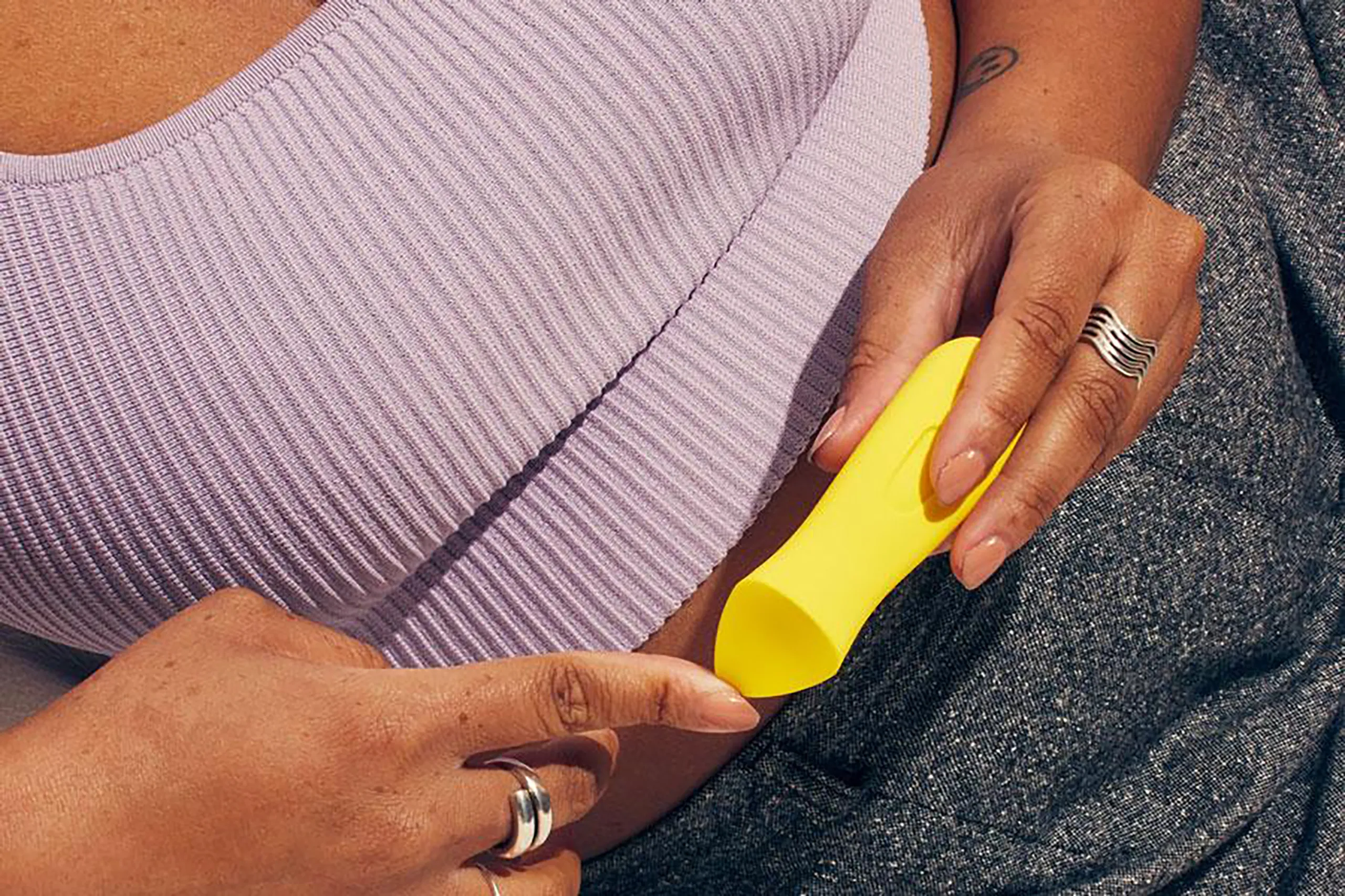 Person holding a yellow Kip sexual wellness device while seated on a sofa