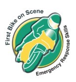 Blood Bikes volunteer in high-visibility gear standing beside a marked motorcycle in a car park near a stone building.