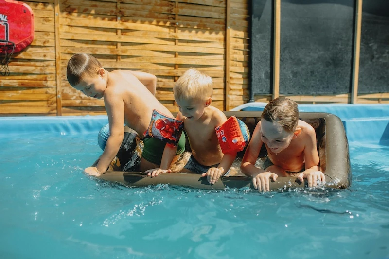 Tres niños divirtiéndose y jugando con inflables en una piscina durante una tarde soleada de verano en familia.