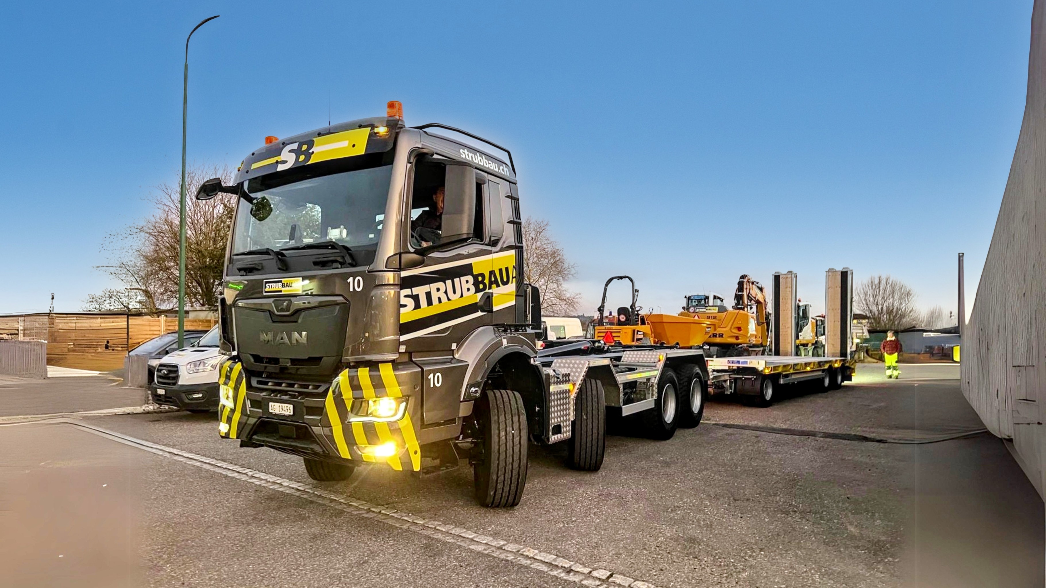 Strub Bau AG transport truck loaded with construction machinery – heavy equipment logistics and site preparation services in Switzerland.