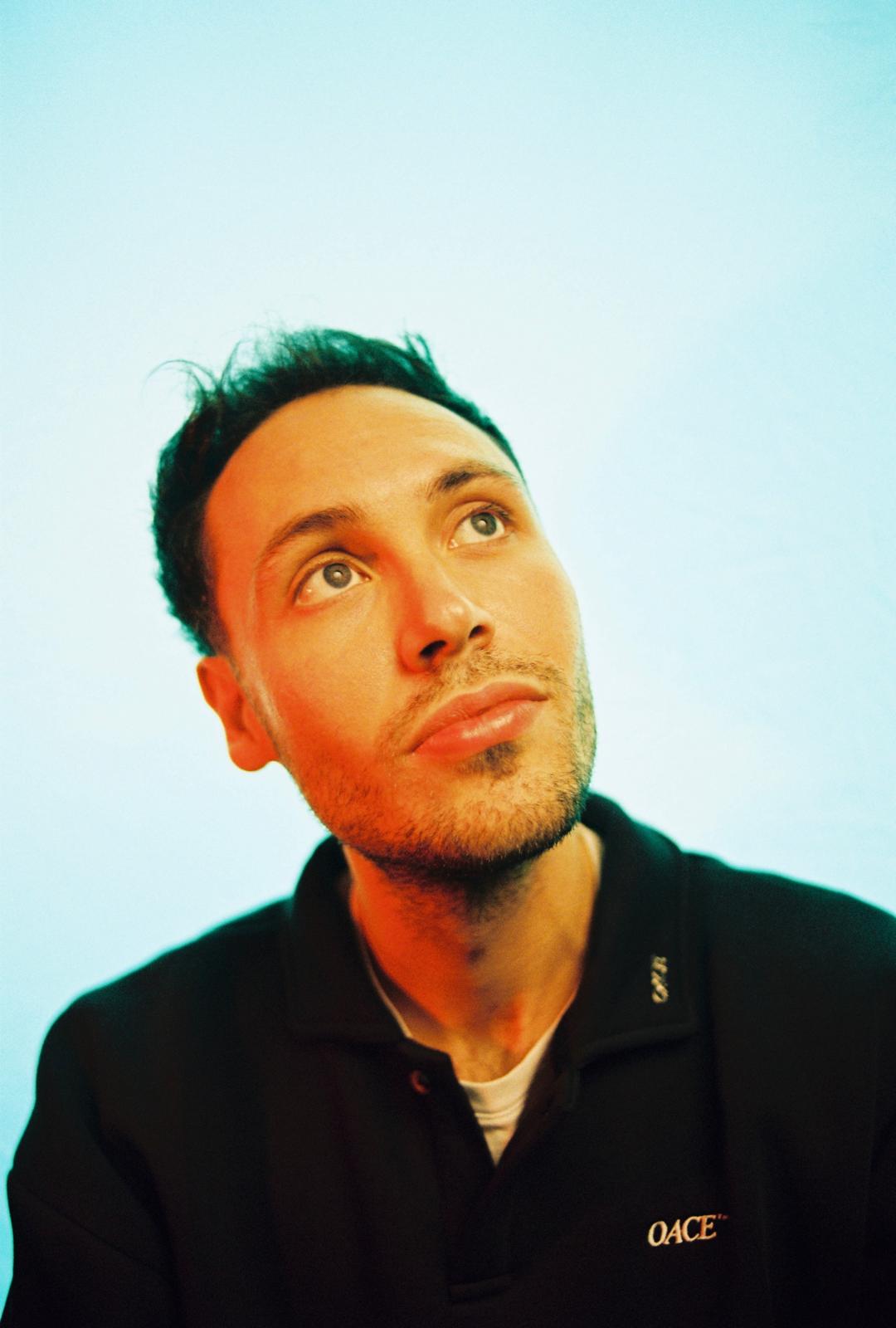 A woman with short curly hair wearing a black t-shirt looks into the camera.