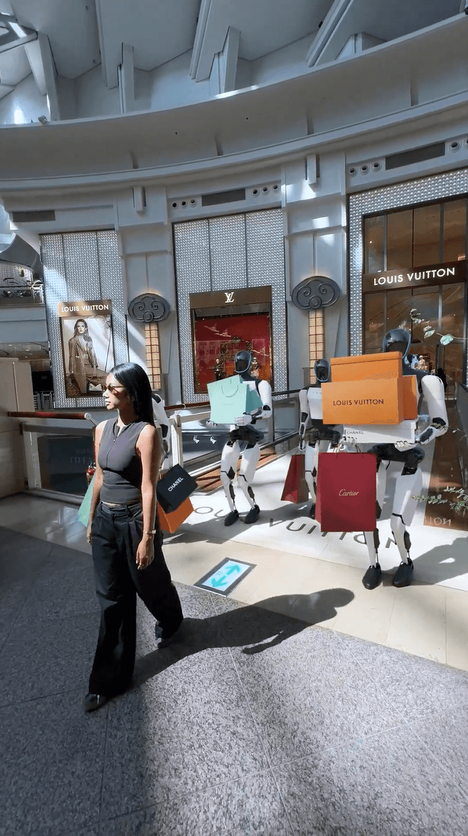 Two robots holding luxury brand shopping bags following a person in a modern mall