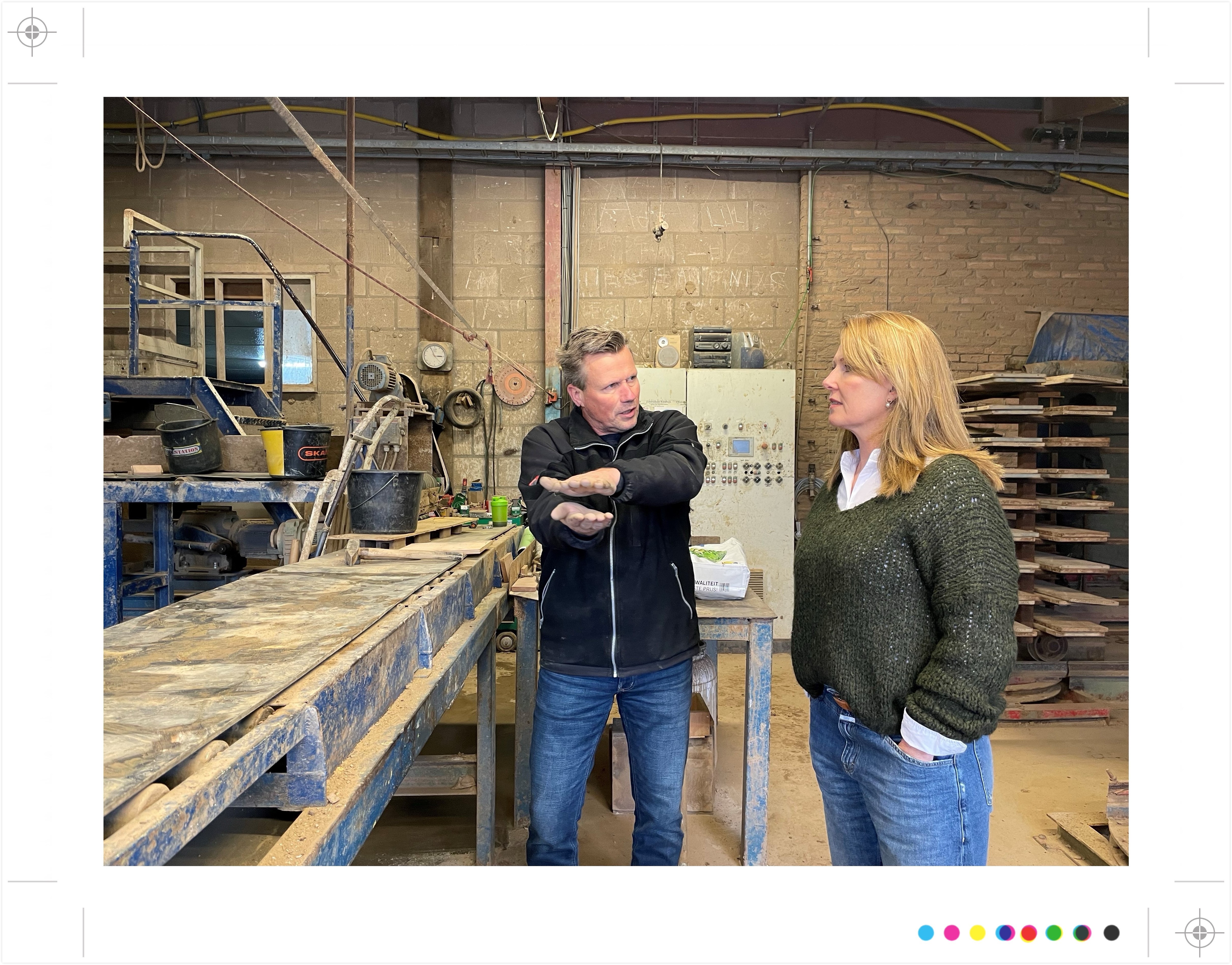 Twee personen in werkplaats, man legt uit aan vrouw, industriele omgeving.
