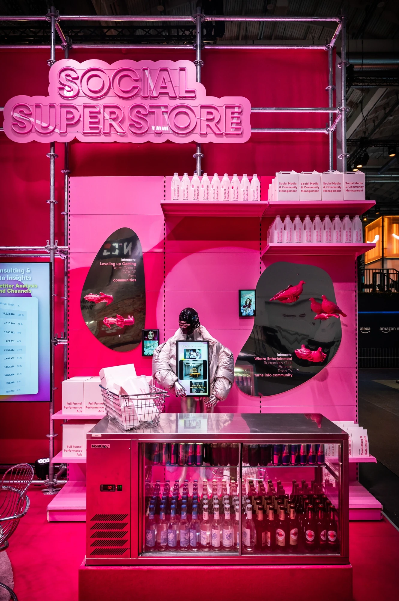 Close-up of the Intermate Social Superstore counter in pink with neon logo, illuminated fridge of bottles and content creator interacting with the display.