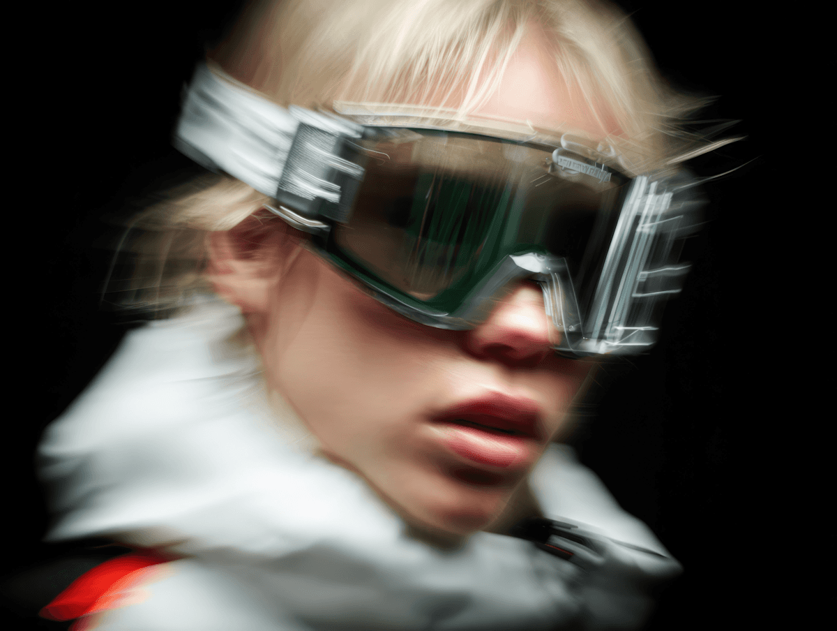 Dynamic close-up of a person in green-tinted goggles and a white jacket, with a blurred effect against a dark background.