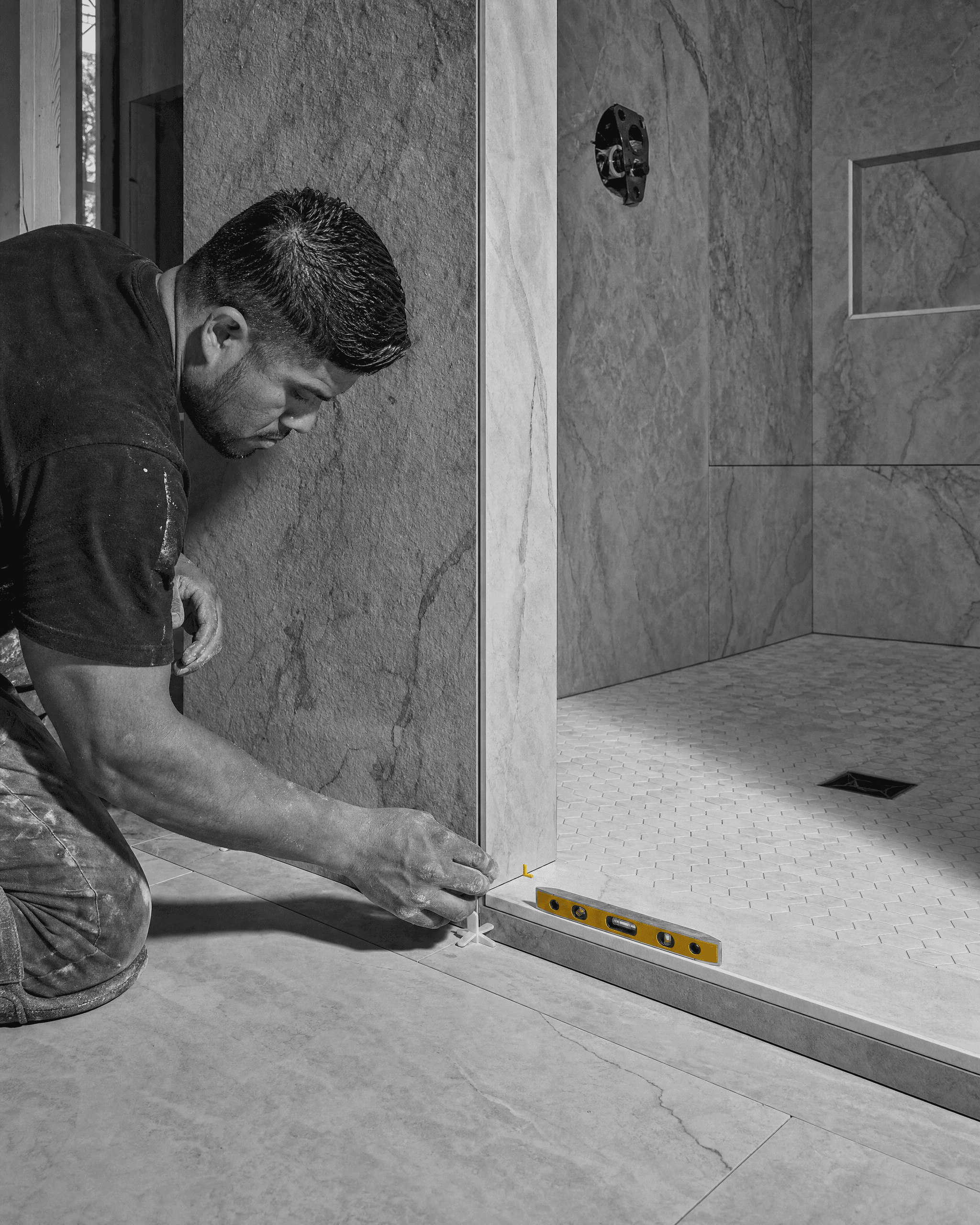 Tile installer setting spacers and checking the shower threshold during a bathroom remodel.