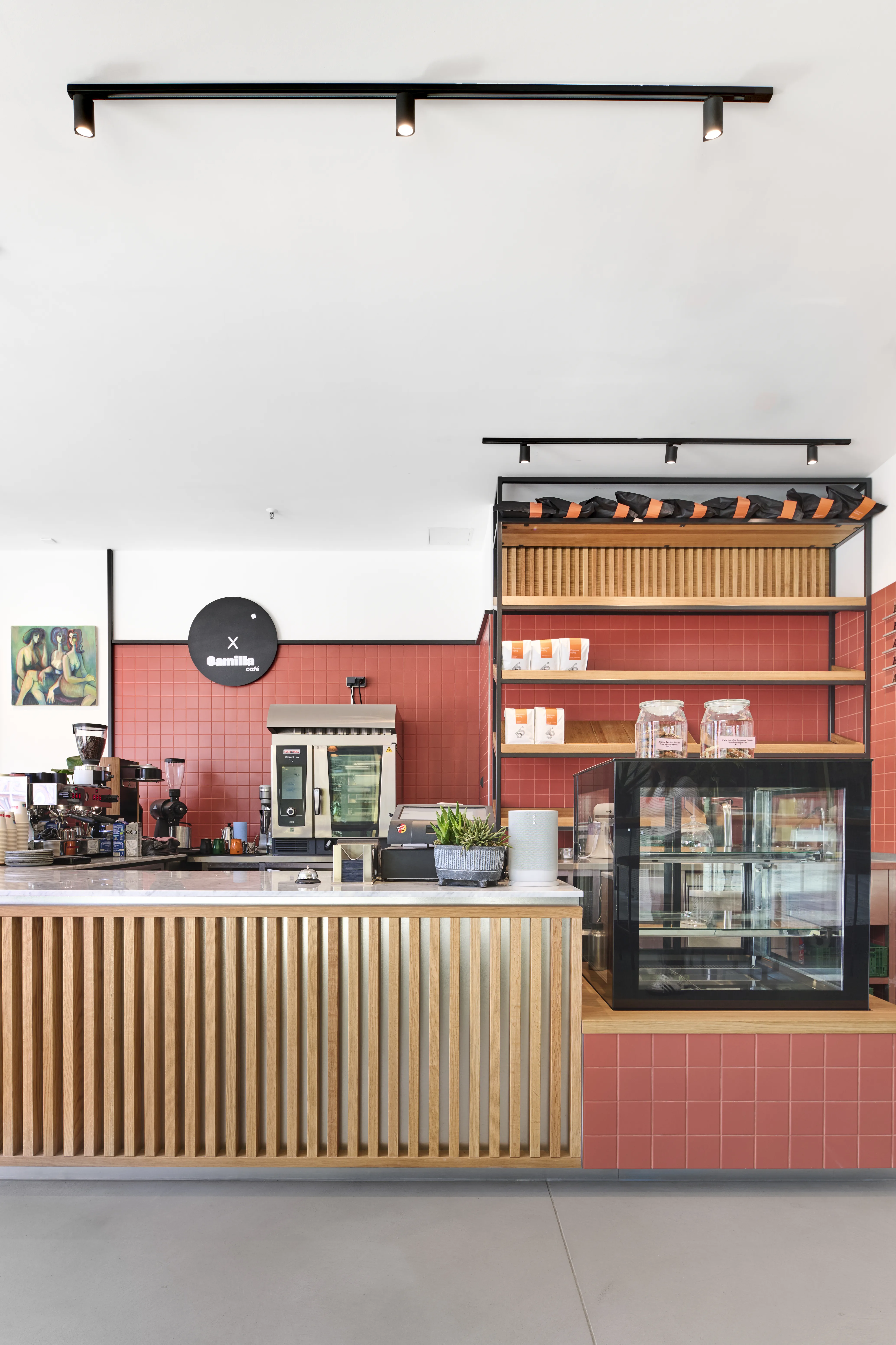 Coffee bar at CAFÉ CAMILLA with menu lettering on the red tiled wall behind the counter and baked goods displayed on the marble top.