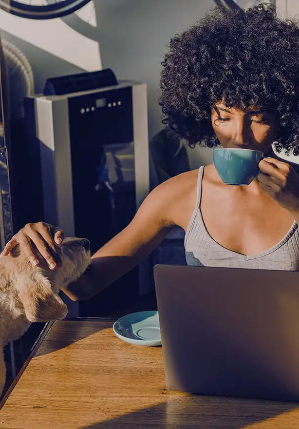 Woman placing an online order on her laptop while drinking coffee and petting her dog
