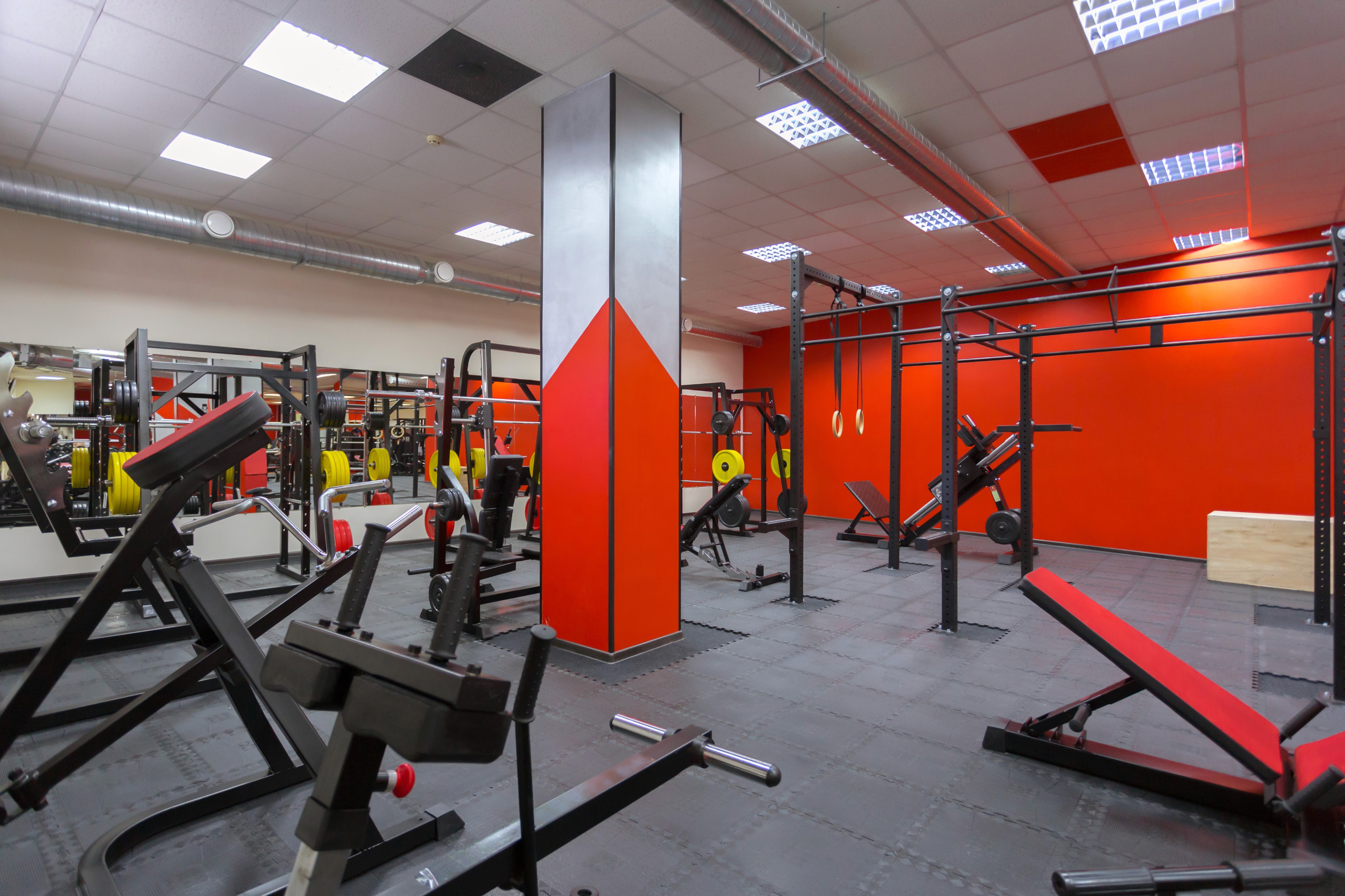 Modern red-and-grey gym interior with various weight machines and benches.