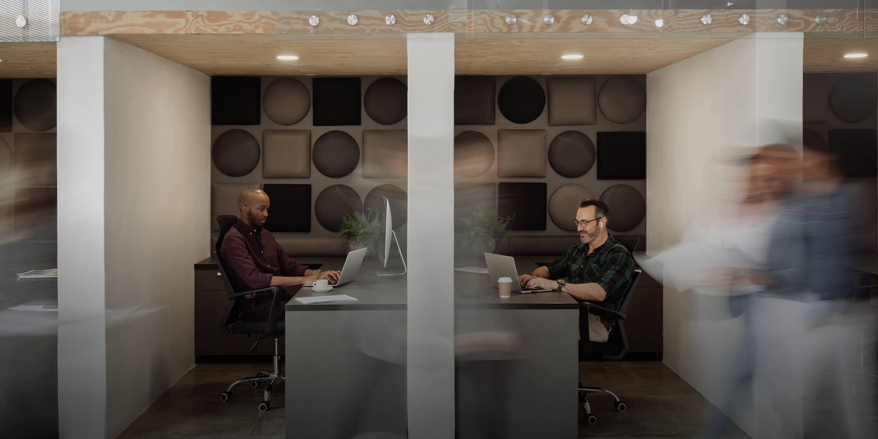 Two men sitting at desks in an office working on laptops