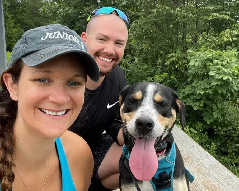 a couple with their dog smiling together at the end of a hike