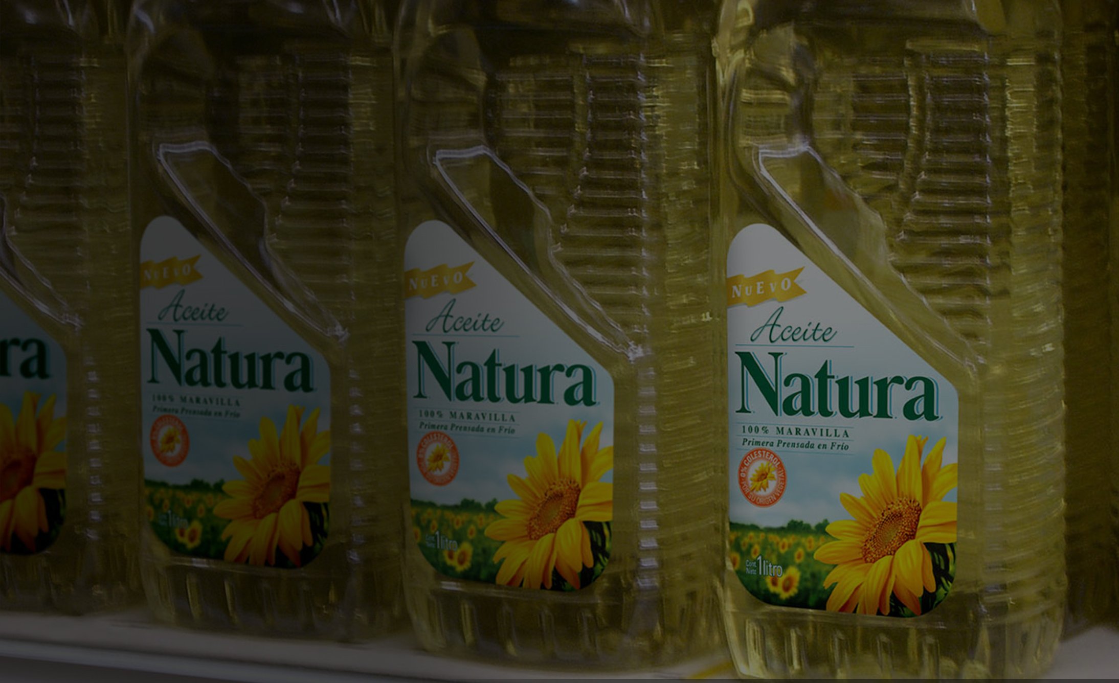 Bottles of Natura sunflower oil are lined up on a shelf. The clear bottles showcase the label featuring a large sunflower and the product name in green text.