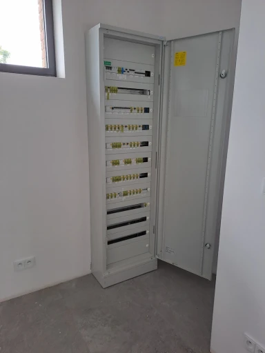 Otevřený elektrický panel s četnými jističi, spínači a kabelovými komponenty, zajišťující rozvod elektrické energie.
